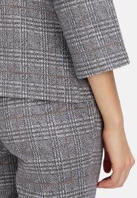 Costume à carreaux gris avec un motif texturé, doté de manches courtes et d'accents bruns, mettant en valeur une silhouette ajustée et des lignes épurées.