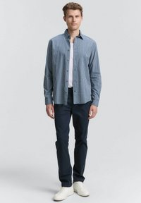 Camisa de cuadros azul con botones, camiseta blanca por debajo, pantalones azul marino y zapatillas blancas. La camisa tiene cuello y mangas largas, con botones por delante.