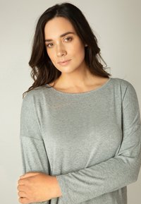 Grauer Langarmoberteil mit lockerem Schnitt und weitem Ausschnitt, hergestellt aus einem weichen, leichten Stoff. Glatte Textur mit dezentem Glanz.