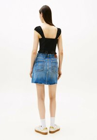 Top nero arricciato con maniche a palloncino, abbinato a una gonna A-line in denim blu. Sneakers bianche con dettagli dorati completano il look.