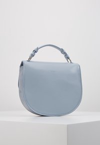 Sac à main en cuir bleu clair avec une forme arrondie, une poignée supérieure et des finitions en argent. Surface lisse avec un minimum de détails de marque.