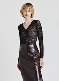 Top in pizzo nero a maniche lunghe con scollatura a V, abbinato a una gonna in pelle lucida marrone scuro a vita alta con tasche laterali.