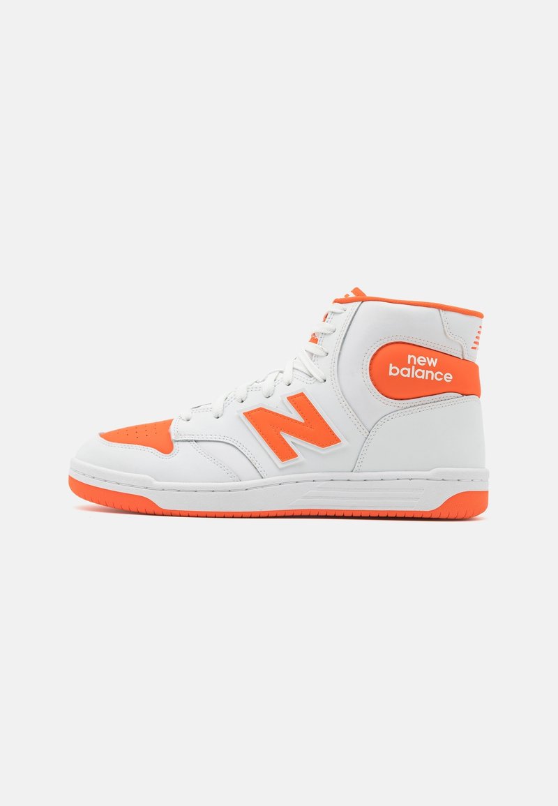 Basket New Balance montante blanc et orange avec logo sur le côté et le talon, présenté sur un fond clair uni.