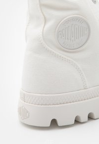 Sneaker alta in tela bianca con finitura testurizzata e suola in gomma. Presenta un logo circolare bianco sul lato, design minimalista.