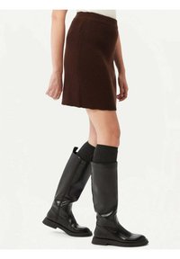 Brun ribbad stickad minikjol med utsvängd nederkant, i kombination med knähöga svarta läderstövlar och grå knästrumpor.