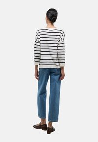 Pull en tricot rayé crème et noir, coupe décontractée avec des manches trois-quarts, associé à un jean droit en toile claire et des chaussures marron.