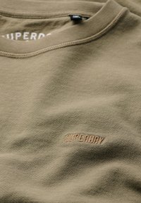 Olijfgroene katoenen sweatshirt met een ronde hals, geribbelde kraag en een geborduurd "SUPERDRY" logo in een lichtere tint. Gladde textuur.
