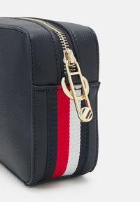 Borsa in pelle testurizzata blu navy con cerniera dorata, caratterizzata da una striscia rossa, bianca e blu; forma rettangolare con dettagli laterali.