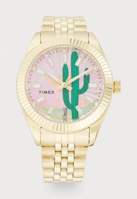 Montre analogique dorée avec un cadran rose à motif représentant un cactus. Bracelet texturé avec fermoir, index horaires rectangulaires et aiguilles dorées.