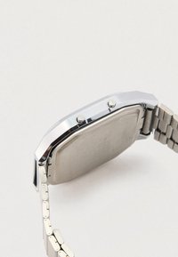 Nerūdijančio plieno laikrodis su oktagono formos korpusu, sidabro spalvos, dviem mygtukais ir šlifuotu metaliniu nugarėle; prijungti metaliniai apyrankės elementai.