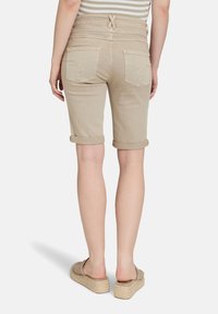 Shorts bermuda en denim beige avec des ourlets retroussés, poches arrière avec des accents cousus, et une ceinture détaillée avec un nœud papillon.