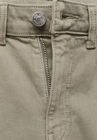 Beiga bomullsshorts med en metallknapp och dragkedja. Har vertikal sömnad längs dragkedjan och förstärkta bälteshällor.