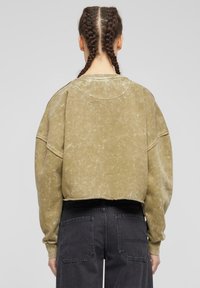Olivově zelená zkrácená mikina s texturovaným povrchem, oversized rukávy, žebrované manžety, kulatý výstřih, doplněná o tmavě šedé kalhoty s kapsami.