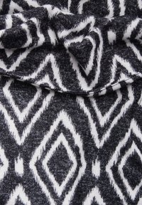 Knitovaná látka s geometrickým vzorem černobílých diamantů s texturovaným, měkkým vzhledem.