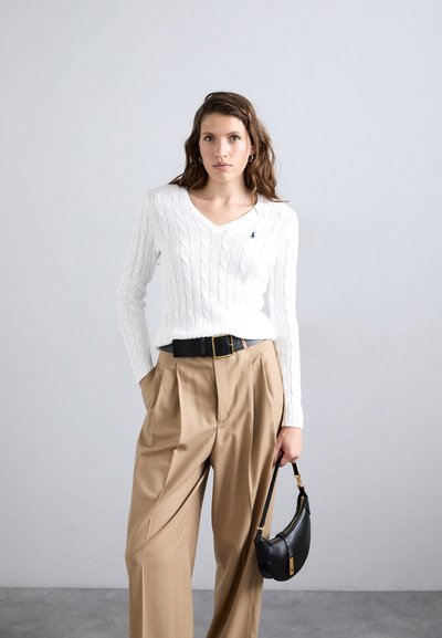 Pull en maille blanche à col en V, associé à un pantalon beige taille haute plissé et un petit sac à bandoulière noir.