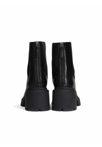 Bottes noires à la cheville avec une finition en cuir lisse, fermetures éclair sur les côtés et semelles en caoutchouc épaisses. Accents de couture double et un léger talon rehaussé.