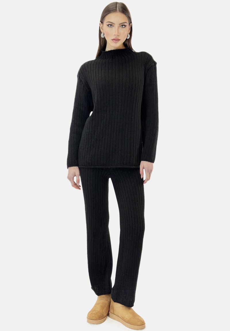 Sort ribstrikket sweater- og bukse-sæt med høj halsudskæring, lange ærmer og en afslappet pasform, kombineret med tanfarvede ruskindsstøvler til anklerne.