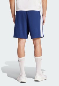 Blå sportshorts med vita sidostrimmor, gjorda av mjukt tyg. Bärs med vita knälånga strumpor och lätta sneakers.