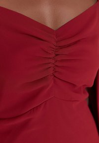 Rotes Kleid aus einem weichen, strukturierten Stoff, mit einem gerafften Design am Ausschnitt und einer eleganten, schulterfreien Silhouette.