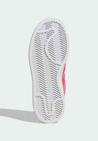 Sola de sapato com uma superfície de borracha branca texturizada, apresentando um padrão em zig-zag e um design ondulado, contrastando com cores de destaque em rosa vivo e laranja.