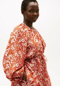 Rotes und weißes Kleid mit floralem Muster, Ballonärmeln und tailliertem Schnitt. Hergestellt aus leichtem Stoff.