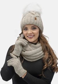Light beige knitted beanie with a fluffy pom-pom, matching gloves and oversized scarf, all featuring a soft texture and ribbed patterns.
