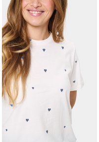 T-shirt en coton blanc à manches courtes, avec des motifs de cœurs bleu marine dispersés. Col rond, texture douce, coupe décontractée.