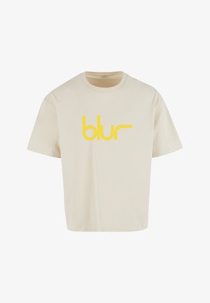 Bézs színű pamut póló kerek nyakrésszel és rövid ujjakkal. A mellkasnál egy feltűnő, sárga "blur" logó található.