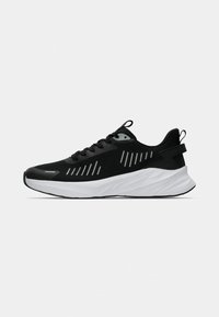 Baskets de sport noires avec fermeture à lacets, semelle blanche épaisse et bandes réfléchissantes sur les côtés et la zone des orteils.