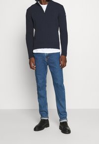 Marineblå ribbad stickad tröja med dragkedja i kragen, ihop med medelblå denimjeans och svarta ankelboots.