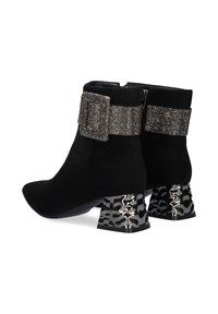 Botines de ante negros con un detalle de hebilla plateada brillante y tacones de bloque metálicos con patrón. Punteras puntiagudas y cierre con cremallera en la parte trasera.