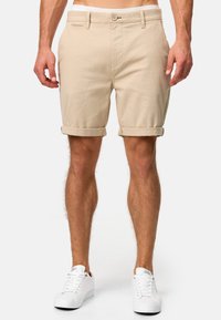 Beige bomuldsshorts med lige snit, opfoldede manchetter, forlommer og en enkelt knaplukning; parret med hvide sneakers.