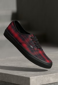 Zapatilla de skate de lienzo a cuadros rojos y negros con suela de goma negra y cierre de cordones. Presenta el logo de Vans en el lateral y una textura suave.