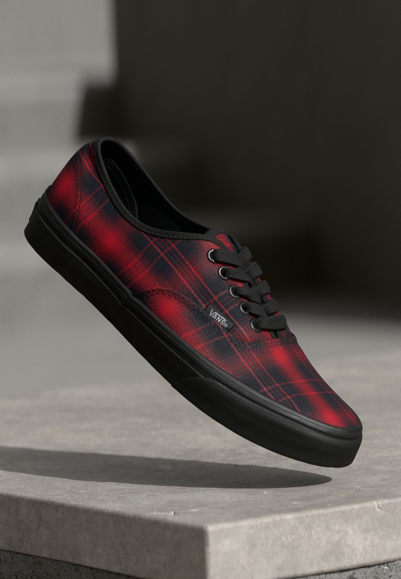 Zapatilla de skate de lienzo a cuadros rojos y negros con suela de goma negra y cierre de cordones. Presenta el logo de Vans en el lateral y una textura suave.