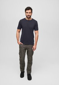 Černé tričko s krátkým rukávem v kombinaci s olivově zelenými cargo kalhotami s bočními kapsami, obuté v černých botách. Jednoduchý design, volný střih.