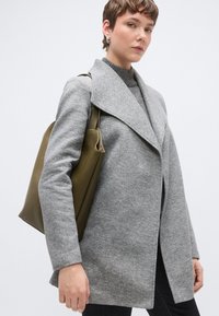 Γκρι παλτό από μείγμα μαλλιού με γιακά με εγκοπές, μακριά μανίκια και άνετη σιλουέτα. Συνδυασμένο με πράσινη δερμάτινη τσάντα.