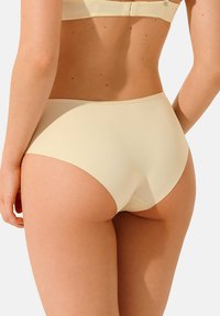 Sous-vêtements taille haute beige fabriqués en tissu lisse, avec un design sans coutures et une couture subtile le long des bords.