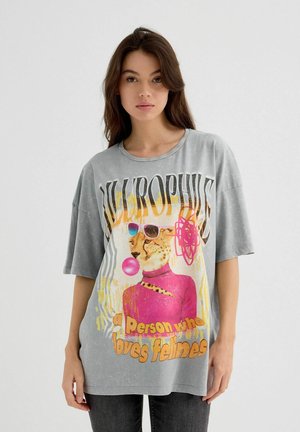 Camiseta de gran tamaño color gris con mangas cortas, que presenta un gráfico de una leopardina con gafas de sol y chicle, con texto colorido debajo.