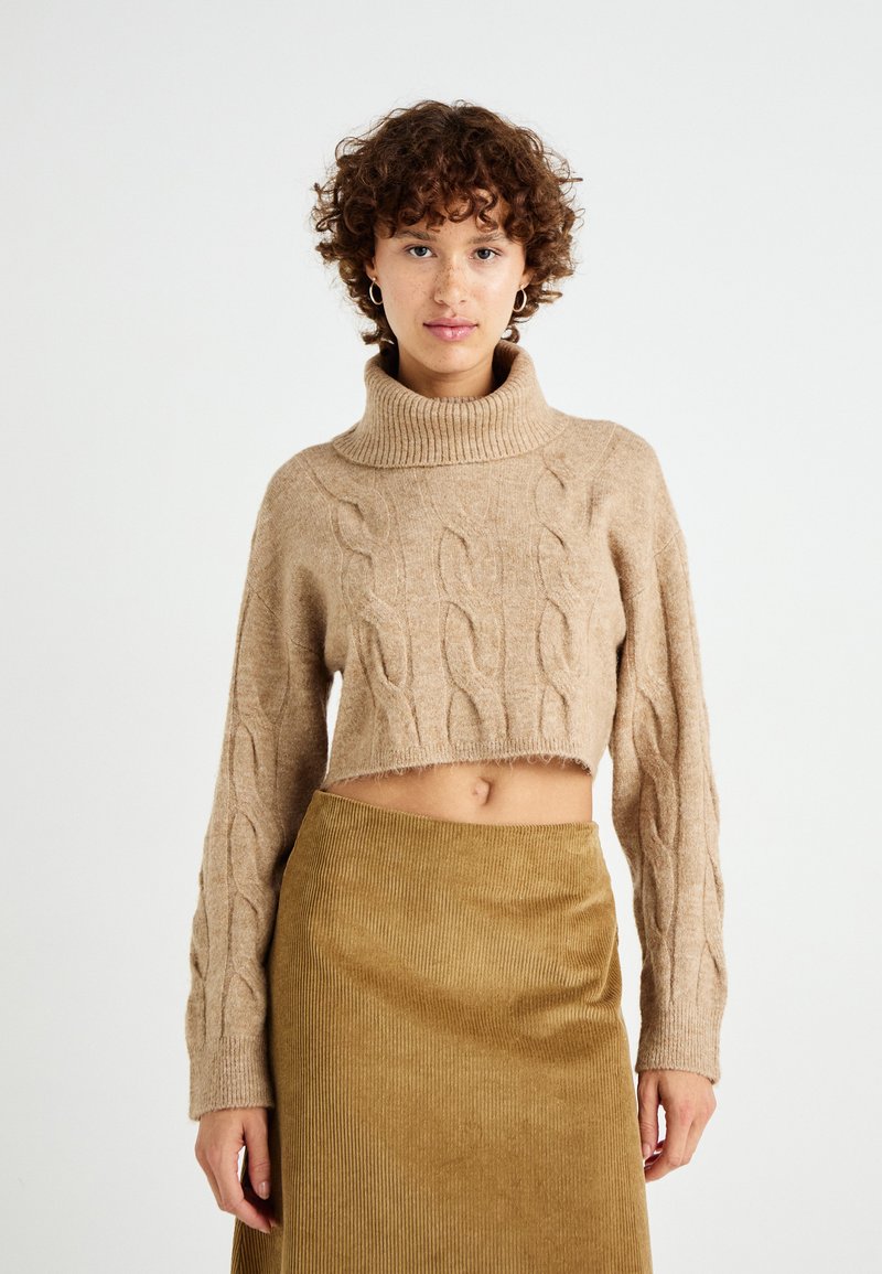 Maglione cropped beige con colletto alto a coste e motivo a treccia, abbinato a una gonna in corduroy verde oliva testurizzata.
