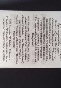 Klistermärke som visar tygkomposition: 64% viskos, 31% polyester, med produktionsdetaljer på flera språk.