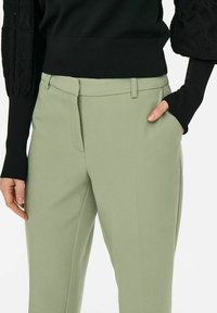Jasnozielone dopasowane spodnie z gładkiego materiału, z wąskim krojem, przednimi kieszeniami oraz paskiem w pasie z szlufkami.