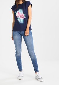 Navyblå kortärmad skjorta med blommönster, matchad med ljusblå slim-fit jeans och vita sneakers. Enkel design, avslappnad passform.