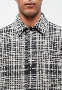 Μαύρο και λευκό πουκάμισο με σχέδιο καρό, πρόσοψη με κουμπιά και μυτερό γιακά, κατασκευασμένο από υφή υφάσματος.