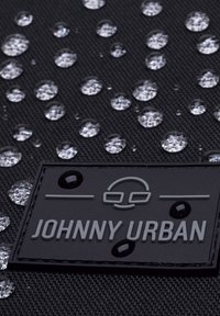 Fekete textil vízcseppekkel. Tartalmaz egy textúrált fekete címkét, melyen a "JOHNNY URBAN" logó dombornyomásos, valamint kör alakú részletek találhatók.