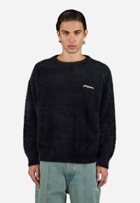 Overdimensioneret sort strikket sweater med en blød, fuzzy tekstur. Har en ribbet halsåbning og manchetter samt et hvidt logo på brystet.