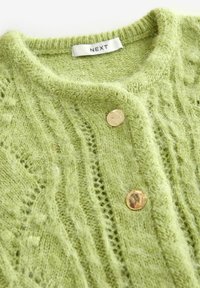 Cardigan tricotat verde cu un model texturat, guler rotund și nasturi aurii. Eticheta spune "NEXT." Material moale și pufoșel.