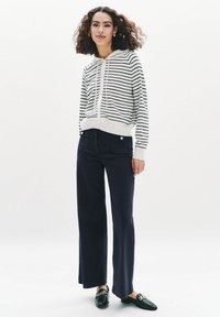 Maglione a strisce con cappuccio in crema e blu marina, con zip frontale, abbinato a pantaloni a gamba larga blu marina con tasche anteriori e dettagli con bottoni.