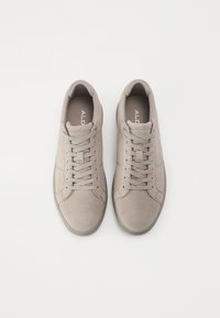 Adidași din suede gri deschis, cu vârf rotund, șireturi plate și o suprafață texturată. Prezintă un design minimal și o marcă subtilă pe limbă.