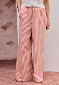 Pantalons larges rayés rose clair avec une taille élastique, ornés de motifs floraux brodés dans une teinte de rose contrastante.
