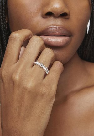 Anillo de plata con múltiples piedras brillantes dispuestas en fila, llevado en una mano de tono de piel claro, mostrando una textura de piel suave.